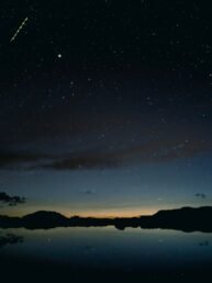 Beautiful silhouette shot of mountains by the river under a starry night sky